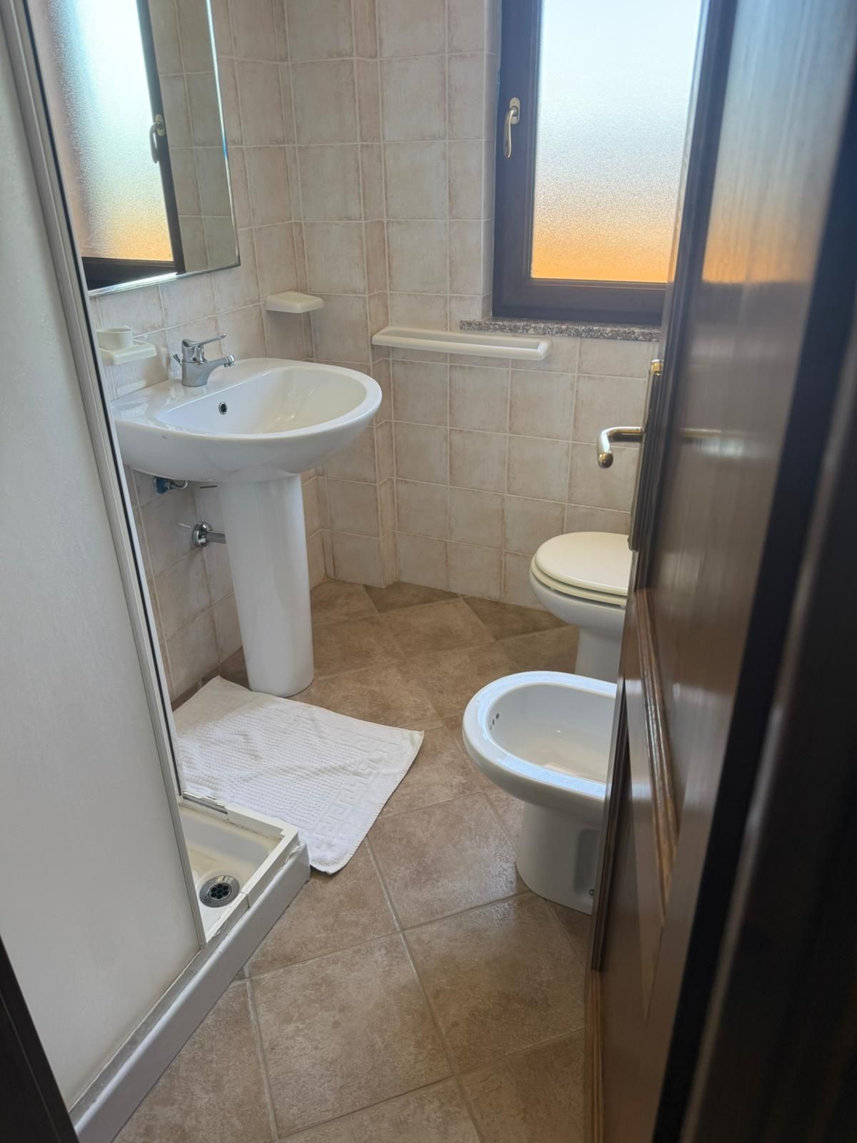 Piccolo bagno con lavandino, WC, bidet, doccia e finestra satinata.