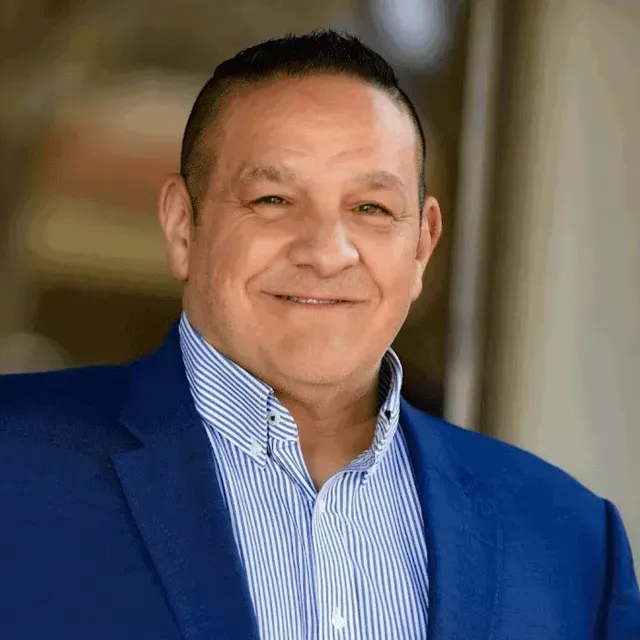 A man in a blue suit and striped shirt is smiling for the camera.