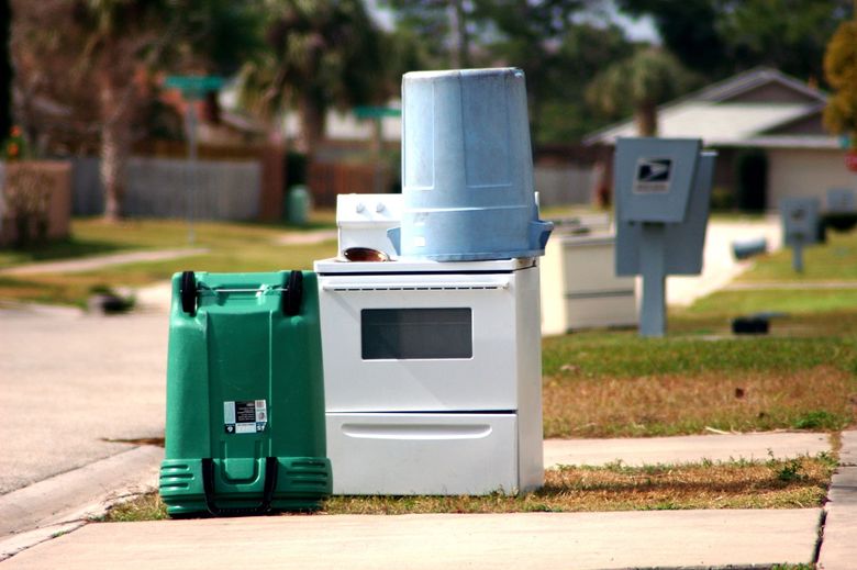 A green trash can is next to a white stove and a blue bucket.