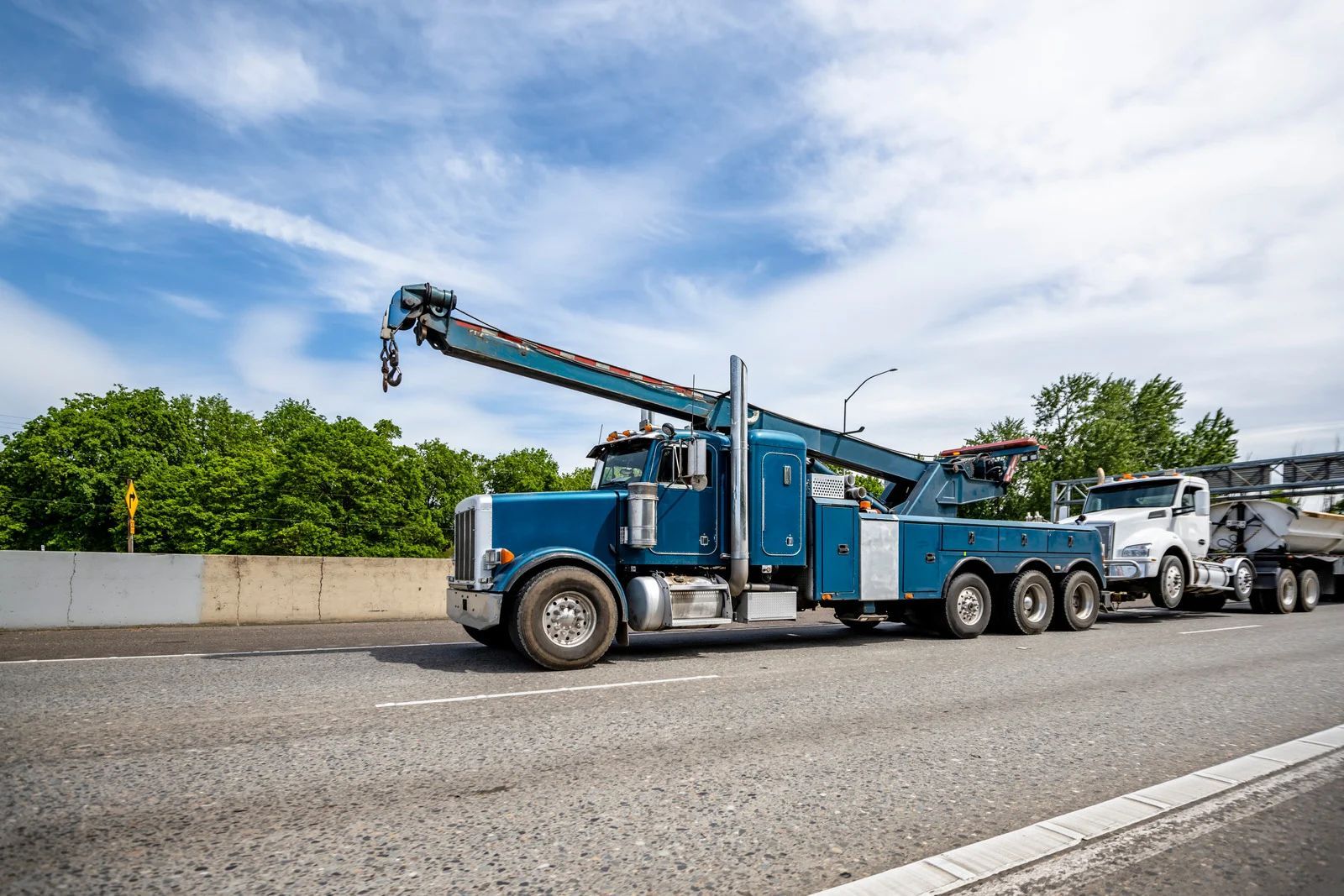 Blue tow truck towing a white car on a highway under a blue sky.