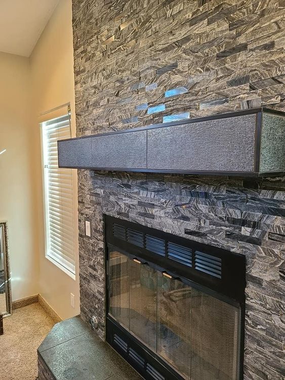 A fireplace with a stone wall and a mantle in a living room.