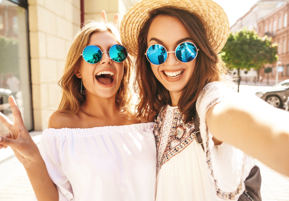 Two women wearing sunglasses and straw hats are taking a selfie.