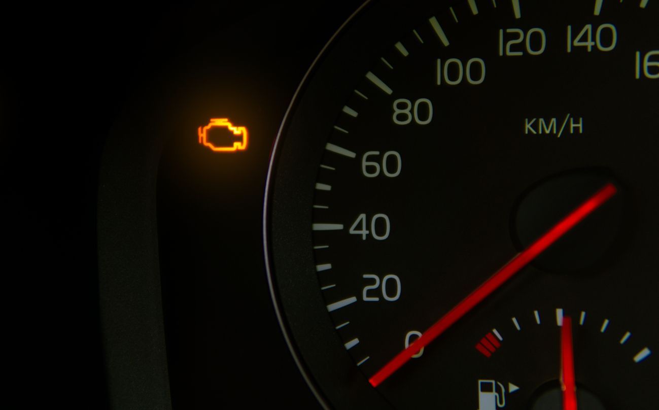 Car dashboard speedometer with a glowing check engine warning light