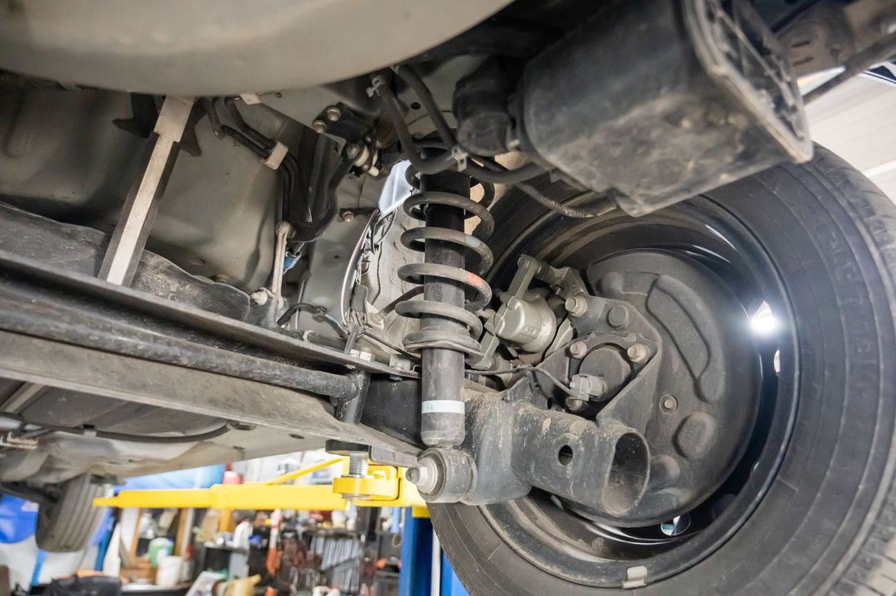 Undercarriage of a car showing suspension, rear wheel, and brake assembly on a lift