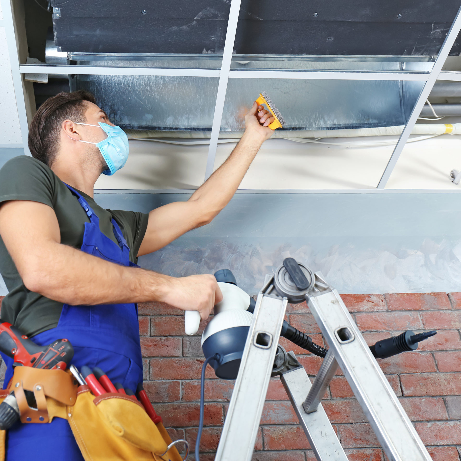 A man in blue overalls is standing in an office with his arms crossed