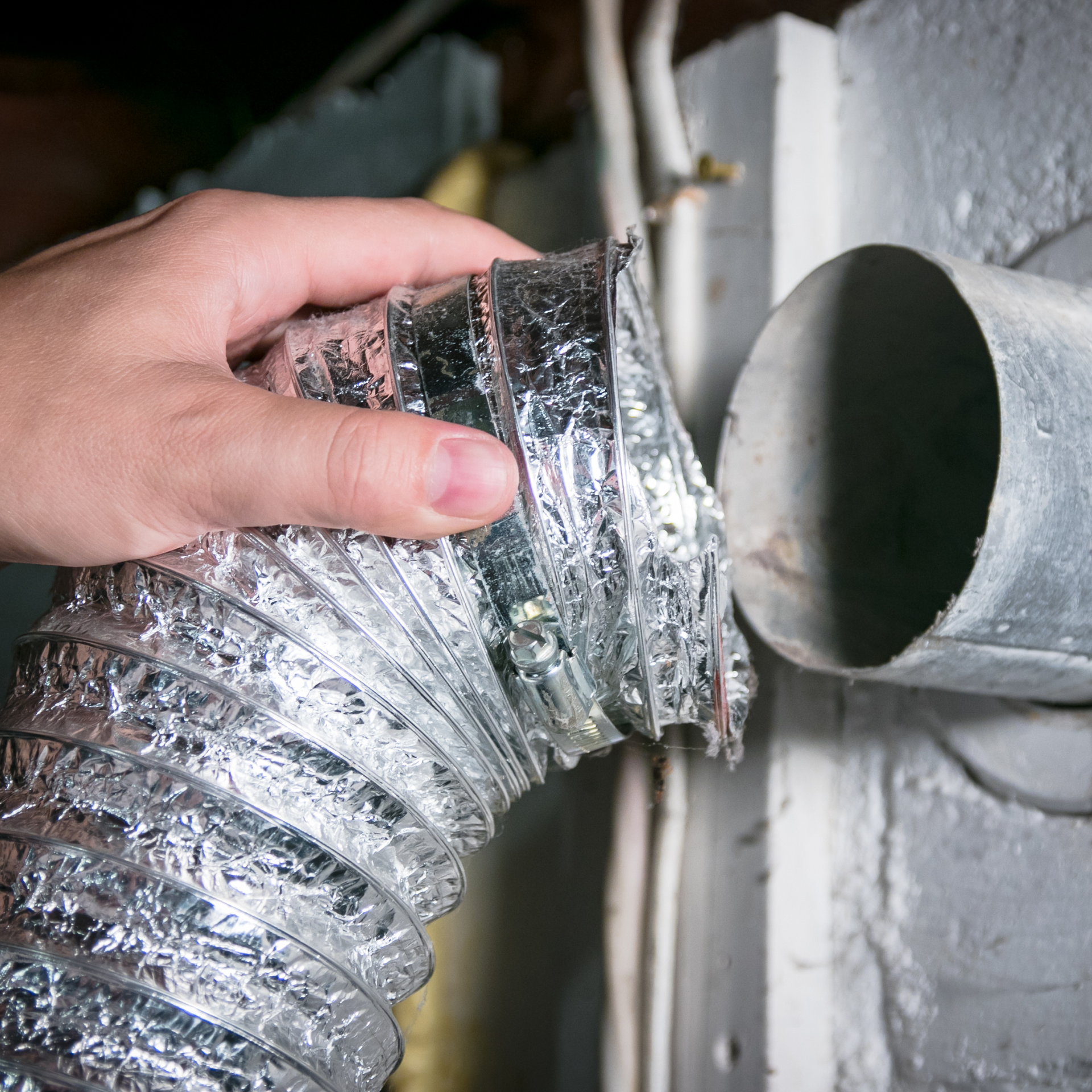 Hand connecting a flexible silver dryer vent hose to a metal vent in a white-painted room.