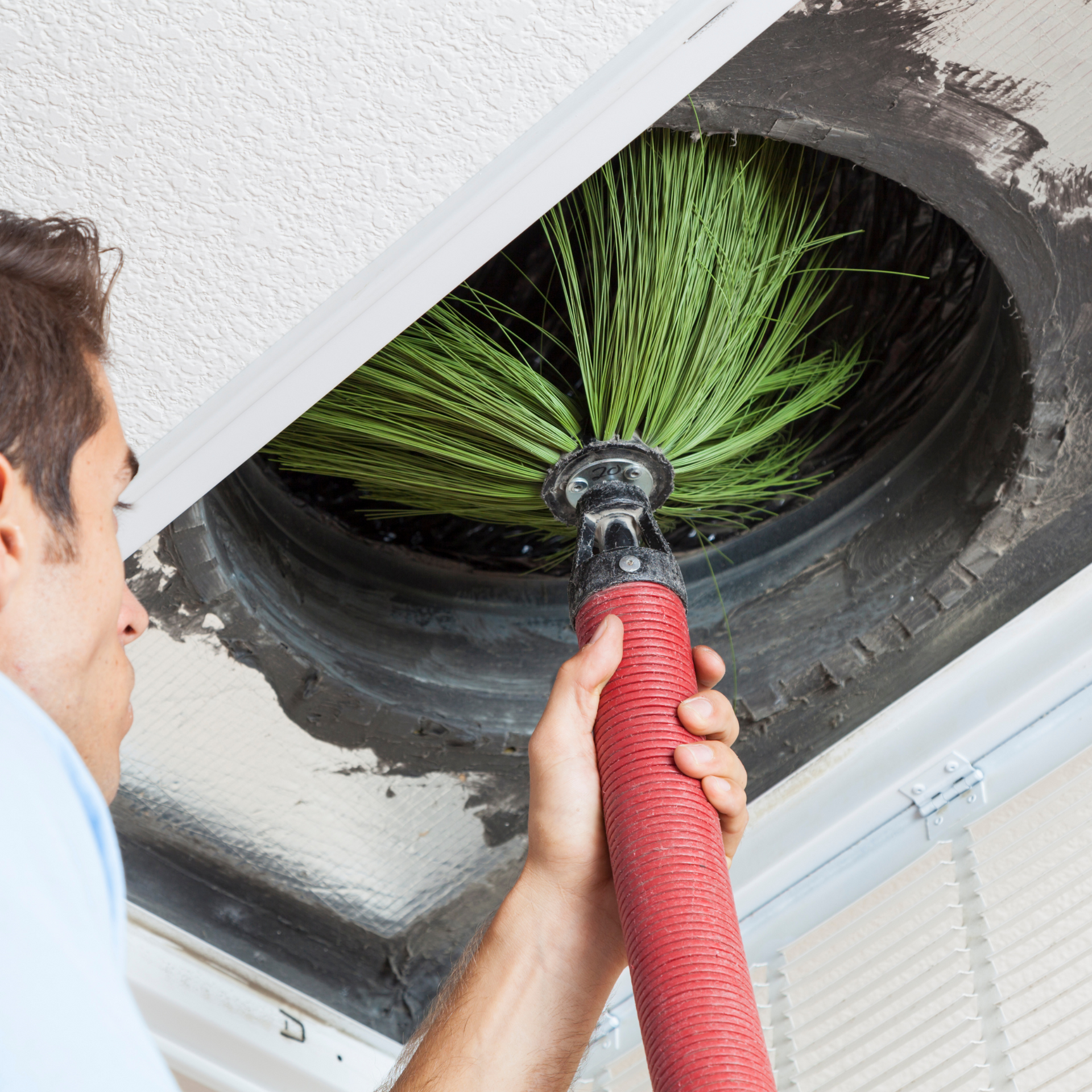Man cleaning an air vent with a large green brush; close-up view inside the vent.