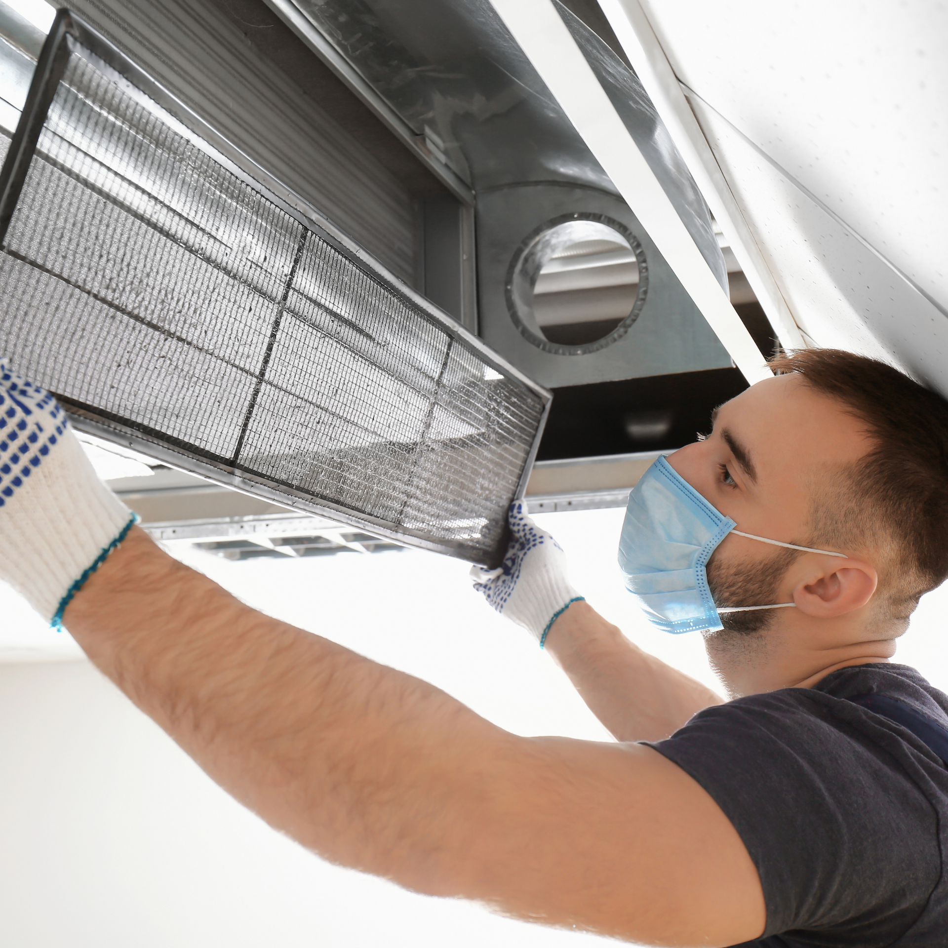 Man in mask and gloves replacing an air filter in a duct.