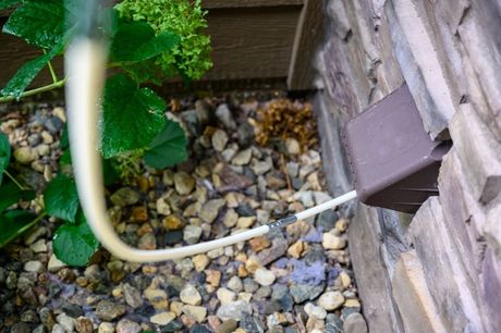 Hand connecting a flexible silver dryer vent hose to a metal vent in a white-painted room.