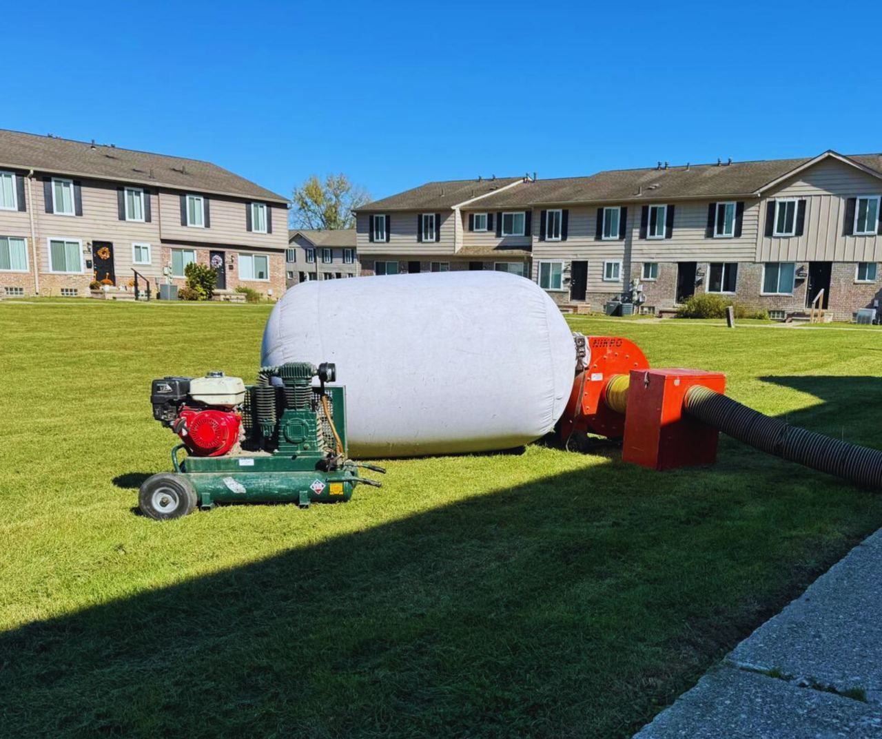 A wood chipper processing a log with a large white bale in a grassy area near apartments.