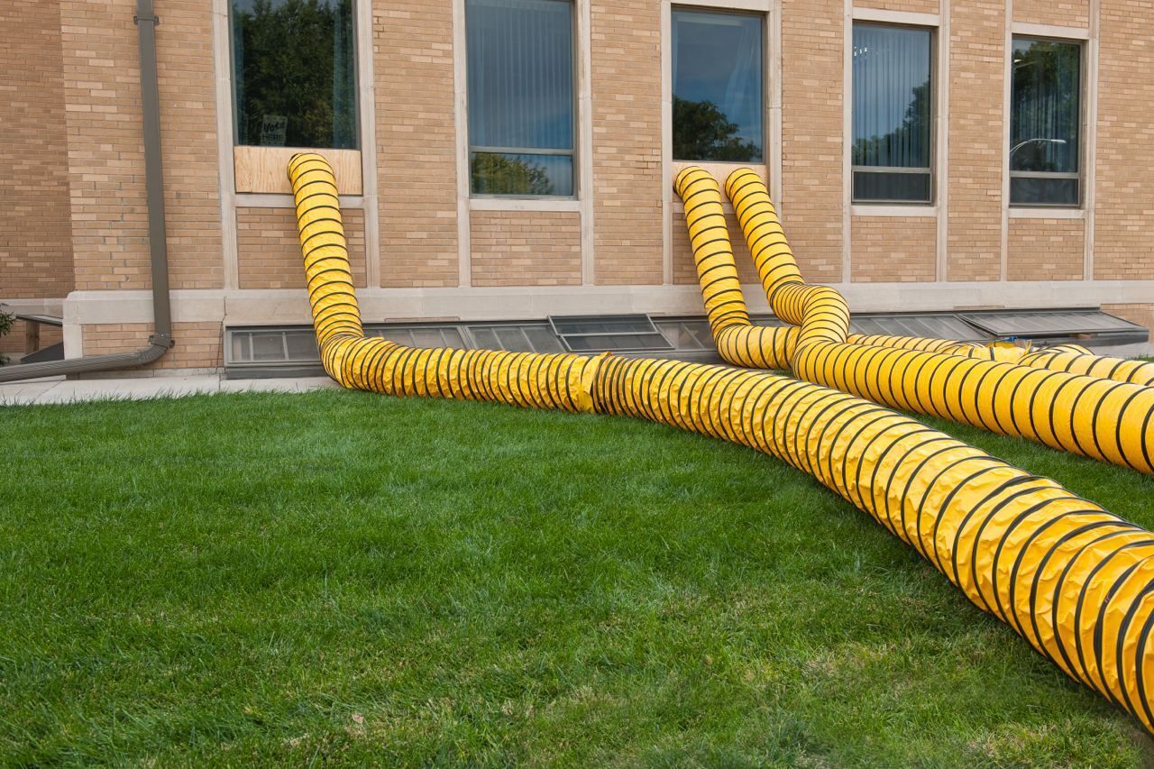Yellow flexible tubes extend from building windows onto a green lawn.