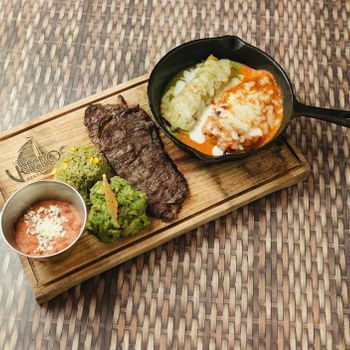 A wooden cutting board topped with a pan of food and a bowl of guacamole.