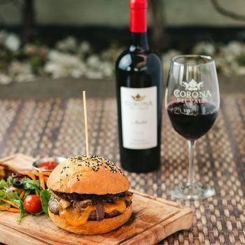 A hamburger is sitting on a wooden cutting board next to a glass of wine and a bottle of wine.