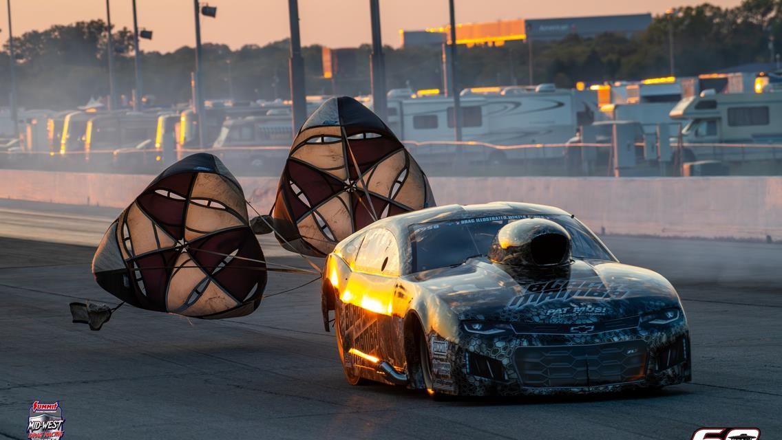 A drag racing car on a track deploying two large, tan and brown parachutes to slow down during a sunset race.