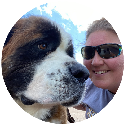 A woman wearing sunglasses is standing next to a large brown and white dog.