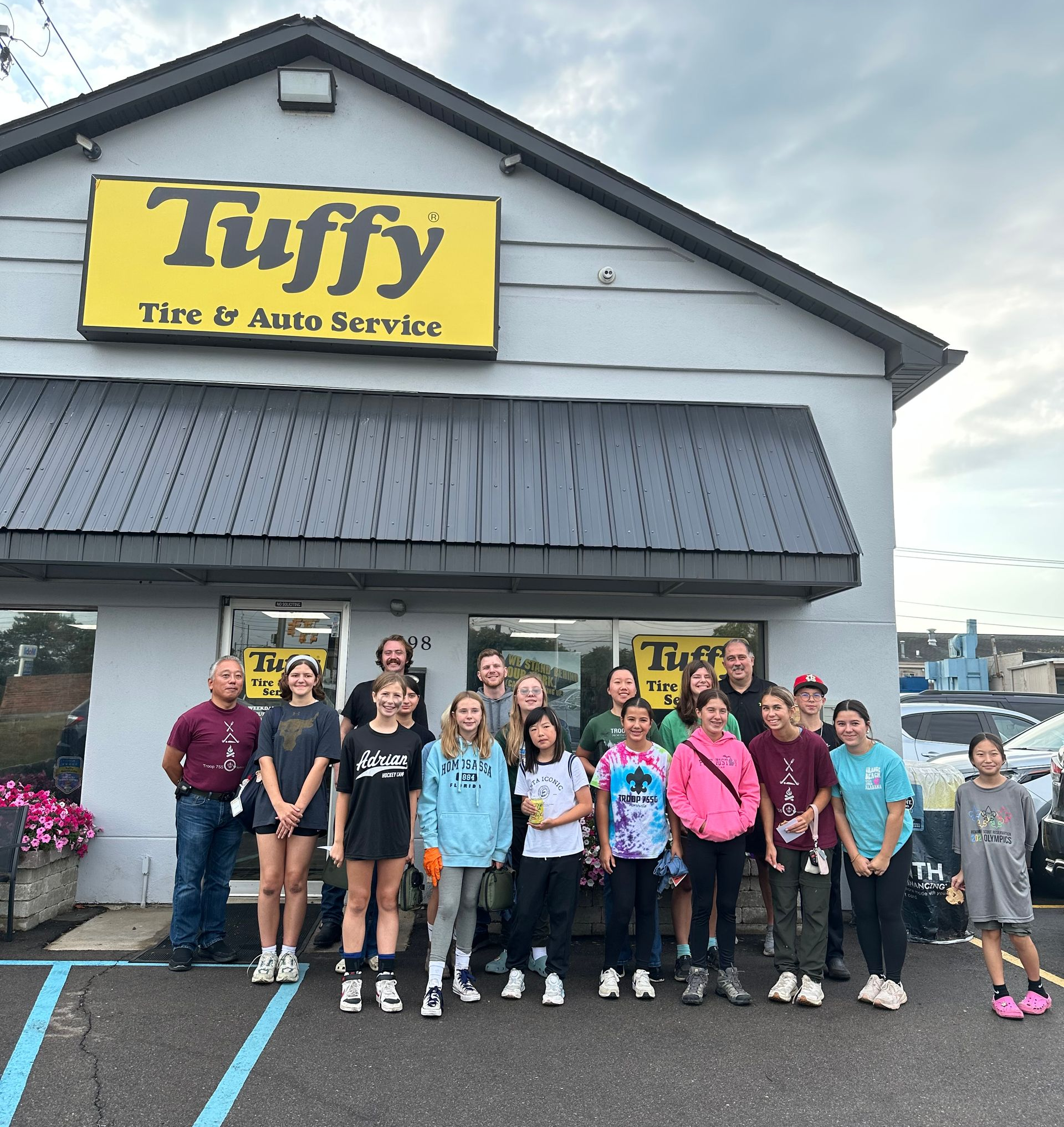 Group of people standing in front of Tuffy Tire & Auto Service shop with yellow sign.