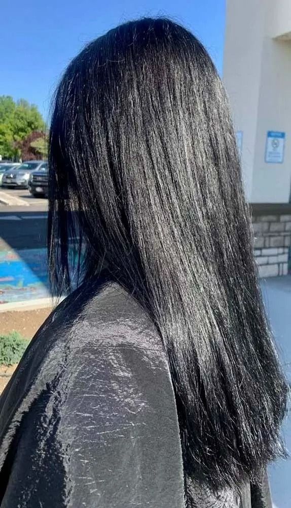 Side profile of a person with long black hair wearing a dark jacket outdoors near a building and pool