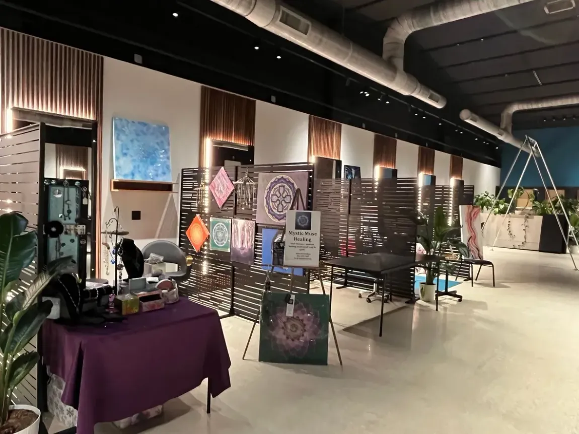 Indoor event booth with purple-draped table, chairs, decorative panels, and potted plants in a modern hall