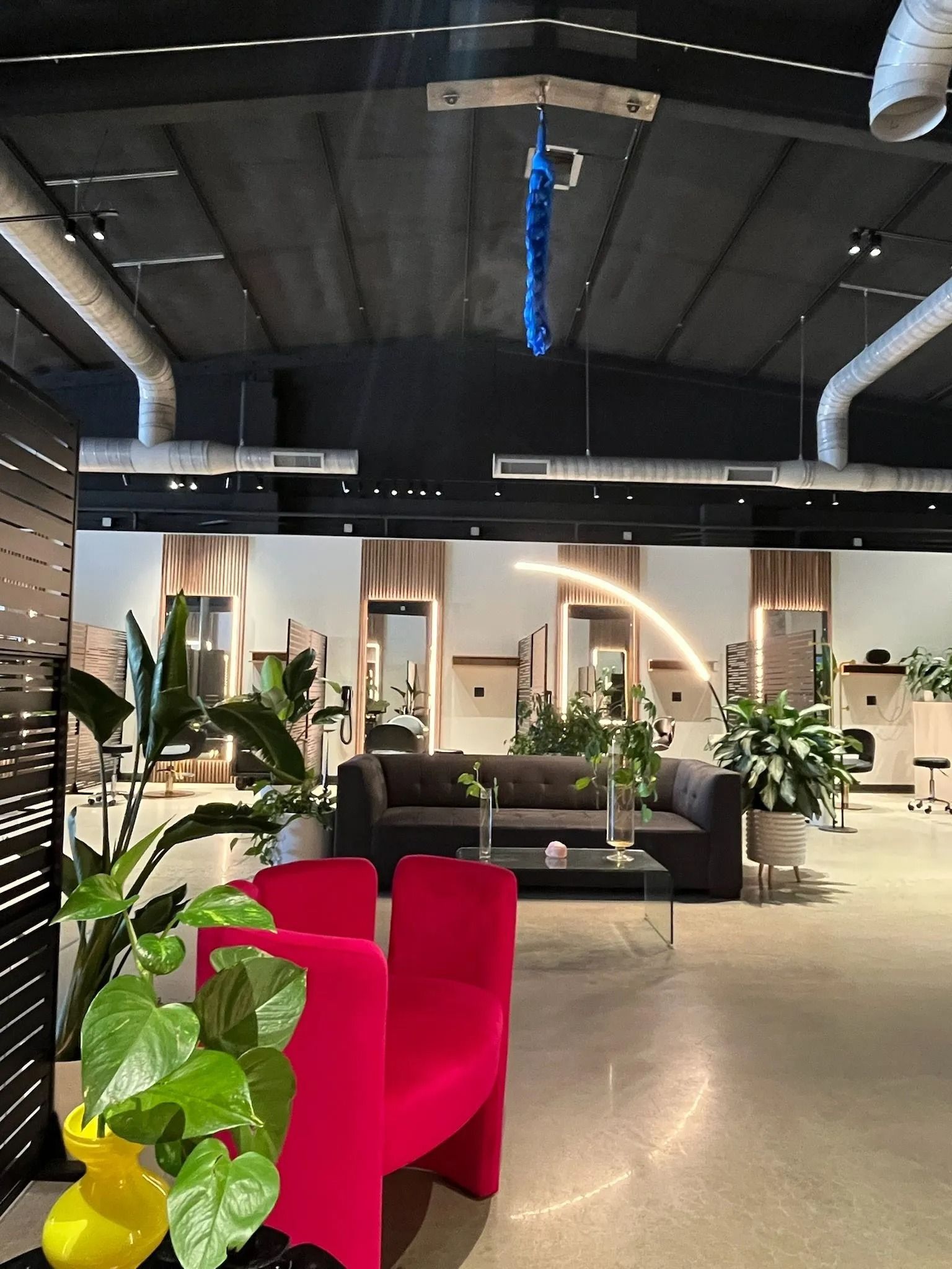 Modern lounge with red chairs, plants, and sofas under a dark arched ceiling
