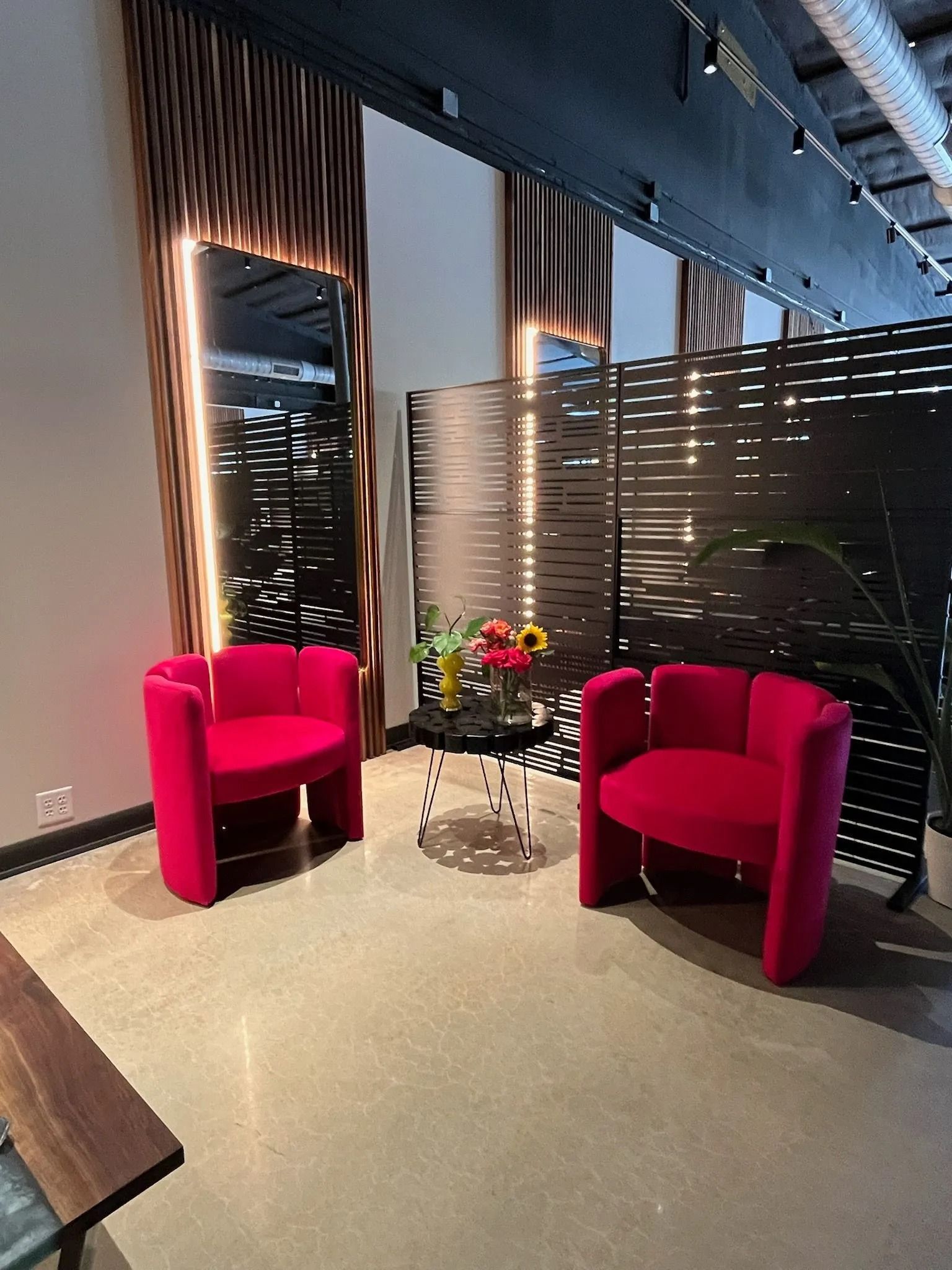 Modern lounge with two bright pink chairs, a small round table, and city views through large windows.