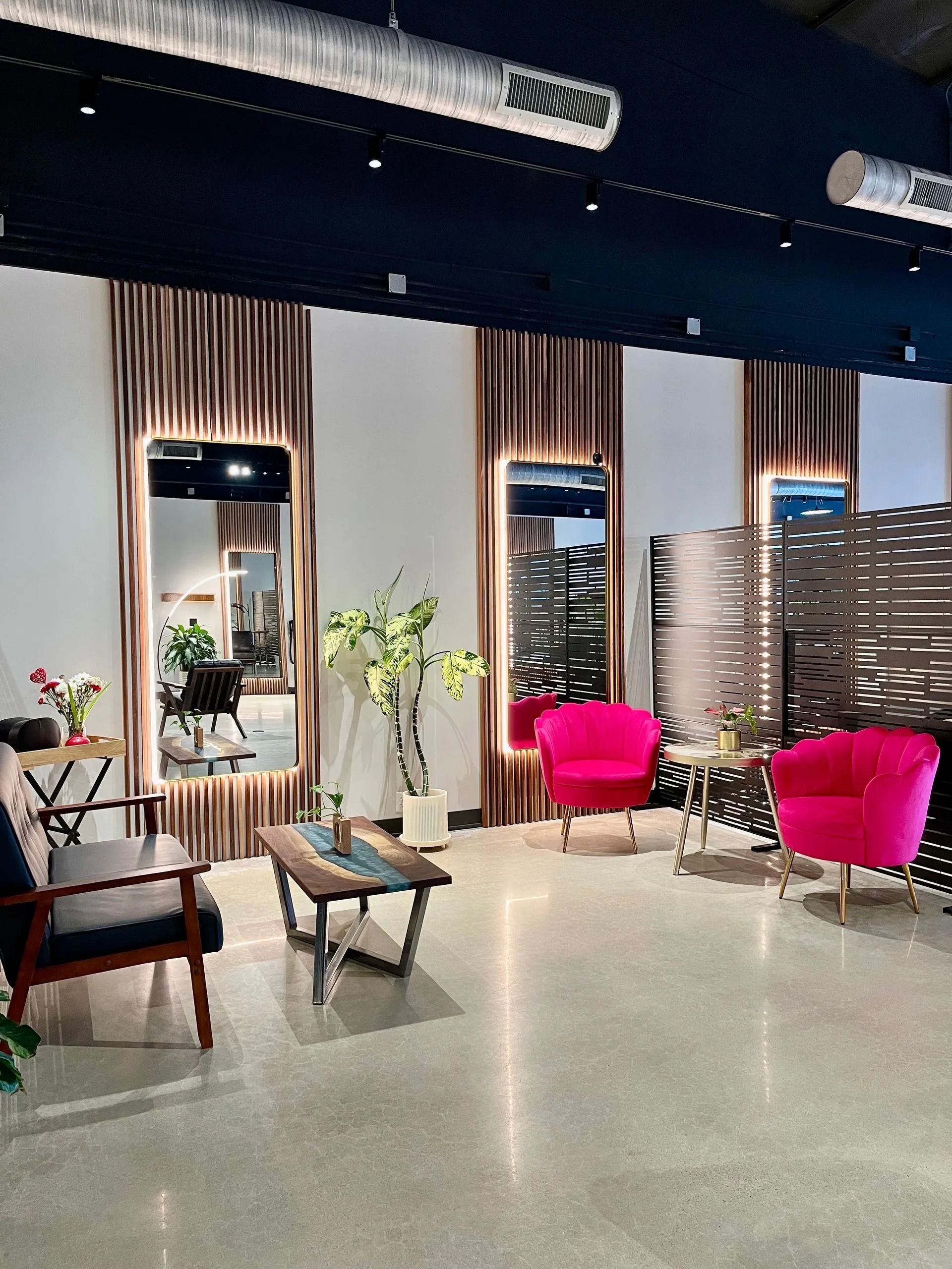Modern lounge with mirrored wall panels, pink chairs, plants, and a bench on a polished floor.
