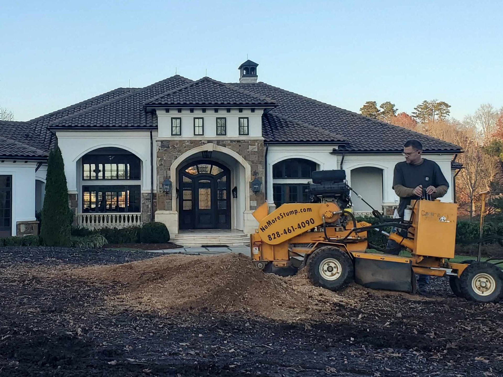 Grinding a stump in front of a house.