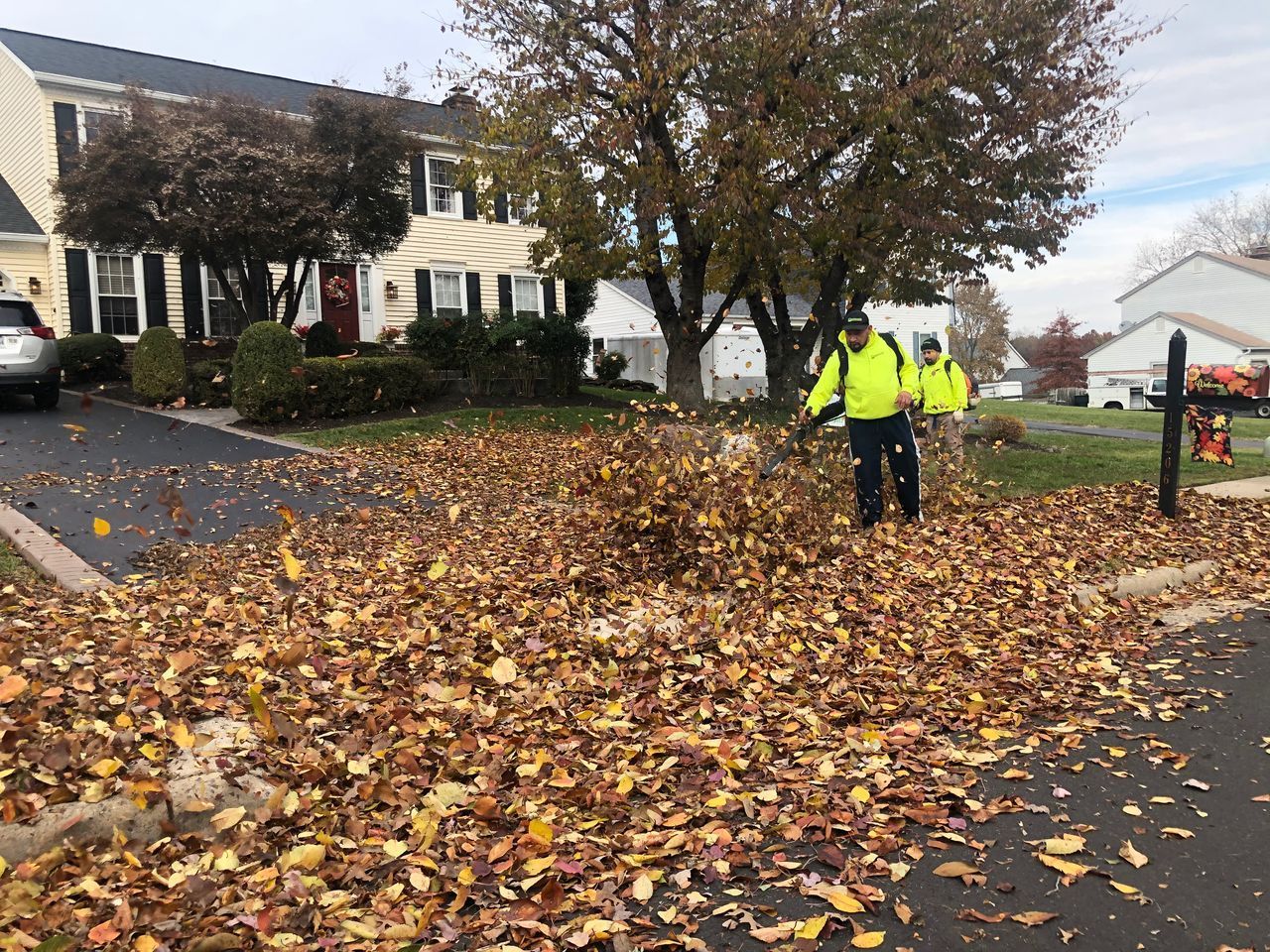 Workers in neon jackets clearing fallen leaves from a suburban street.