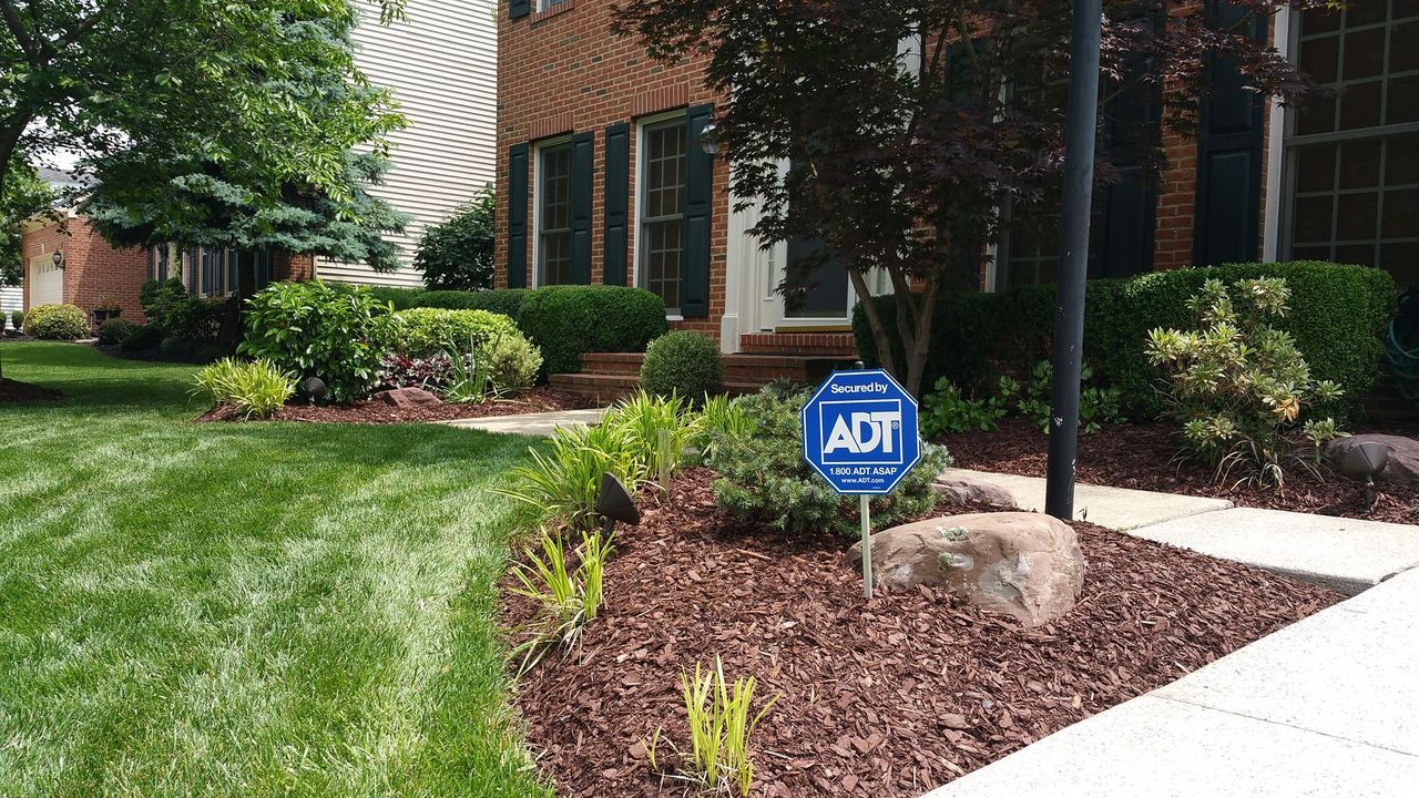 Front yard landscaping with mulch, shrubs, a tree, and an ADT security sign by a brick building.
