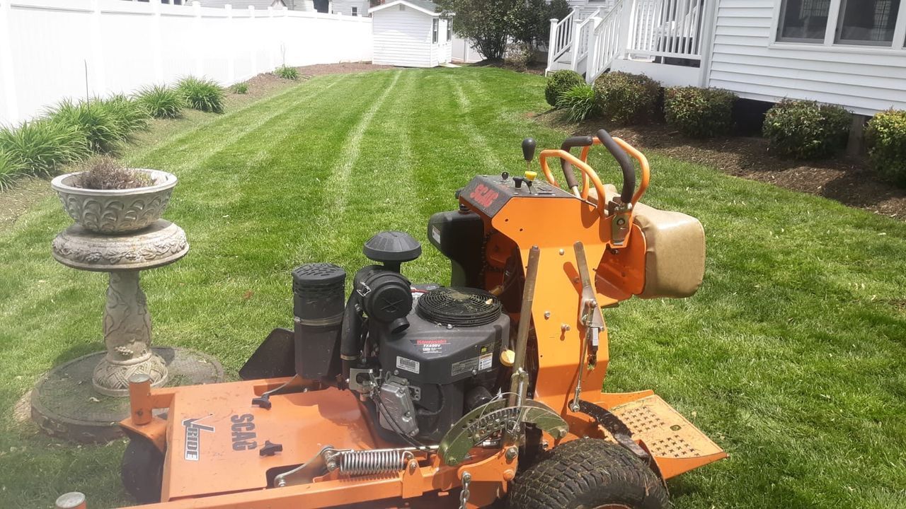 Orange lawn mower on a green grassy yard beside a white fence and house.