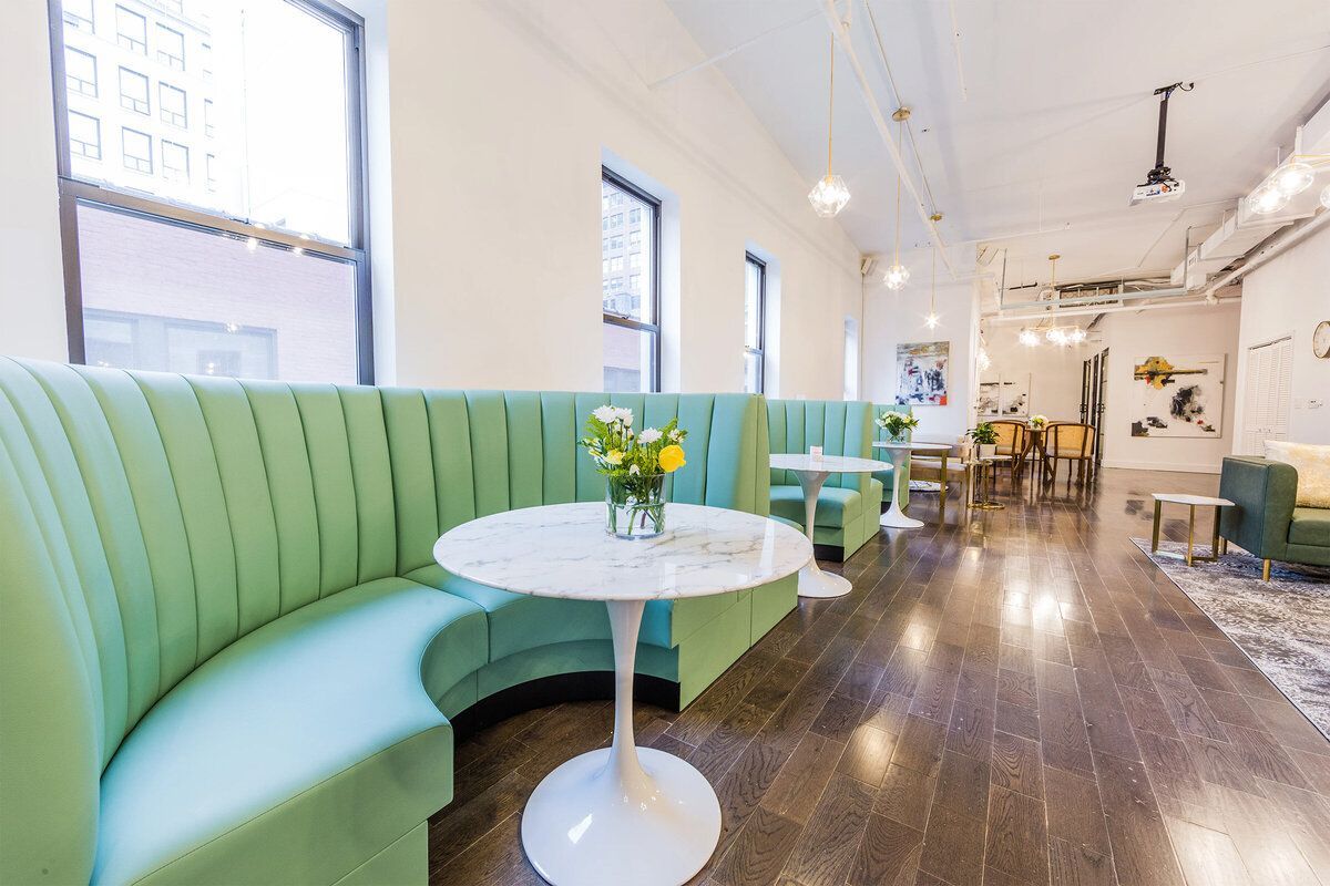 A modern lounge with a curved green booth, marble tables, and wooden floors.