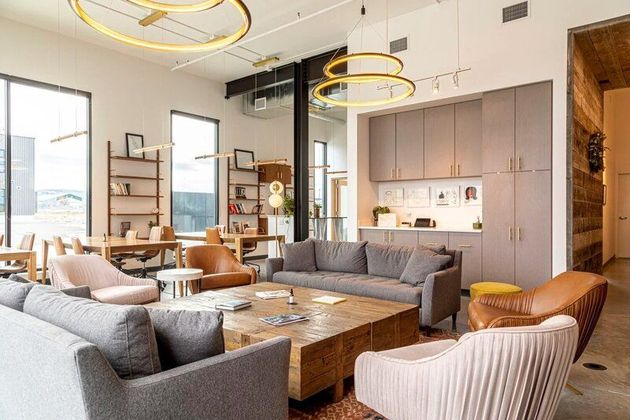 Modern office lounge with gray sofas, armchairs, wood coffee table, and built-in storage.