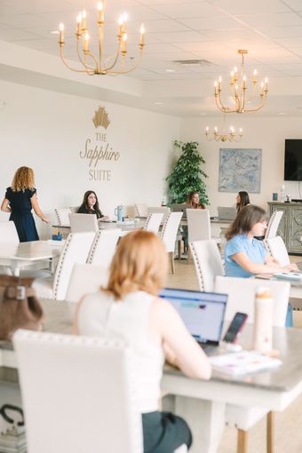 People working on laptops at tables in a bright, modern office space with chandeliers and a plant.