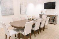 Formal dining room with long table, white chairs, artwork, TV, and console.