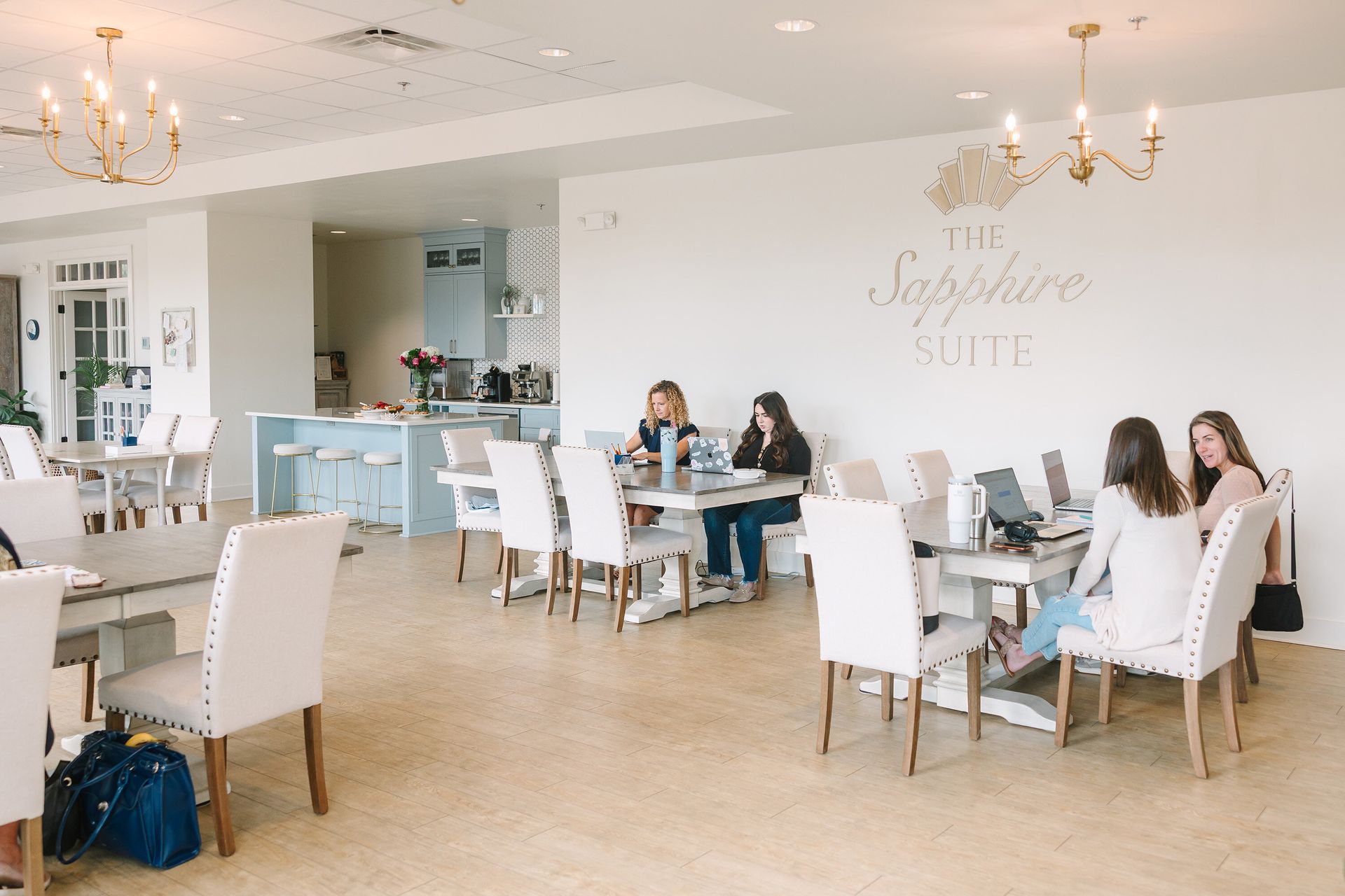 People working on laptops at light-filled tables in a bright, modern co-working space.