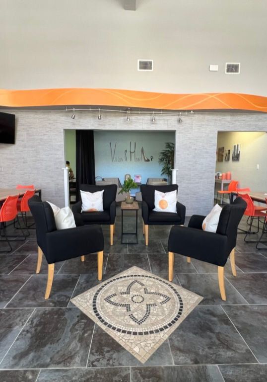 Four black armchairs around a mosaic tile rug in a room with orange accents and tile floor.