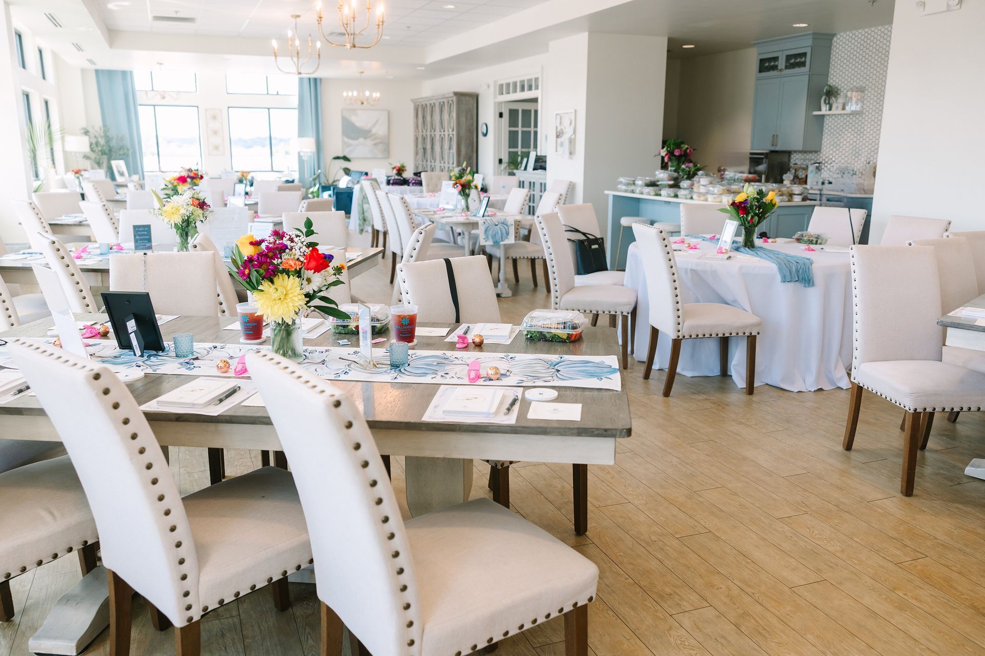 Elegant, light-filled dining room set for a party, with tables, chairs, and floral centerpieces.