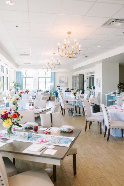 Bright, airy dining room with tables set for a party, decorated with floral centerpieces and light blue accents.
