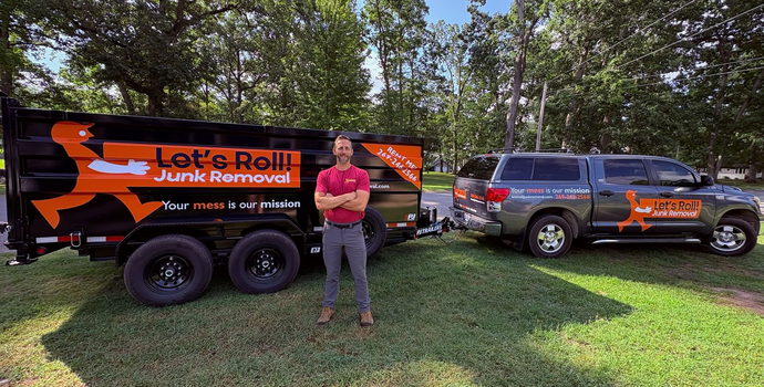 The owner of Let's Roll Junk Removal is standing in front of a dump trailer that says let 's roll.