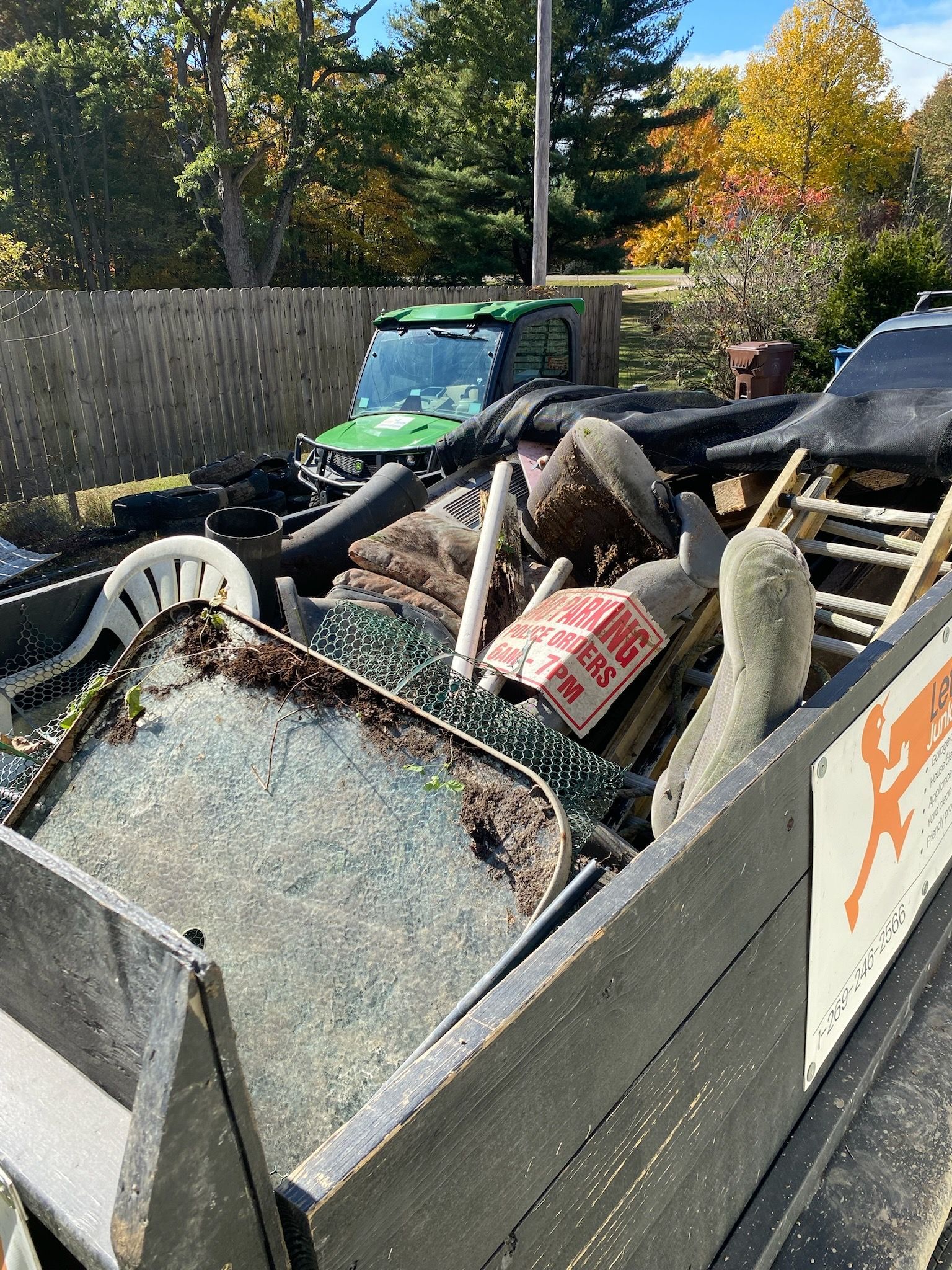 A trailer filled with junk is parked in front of a fence.