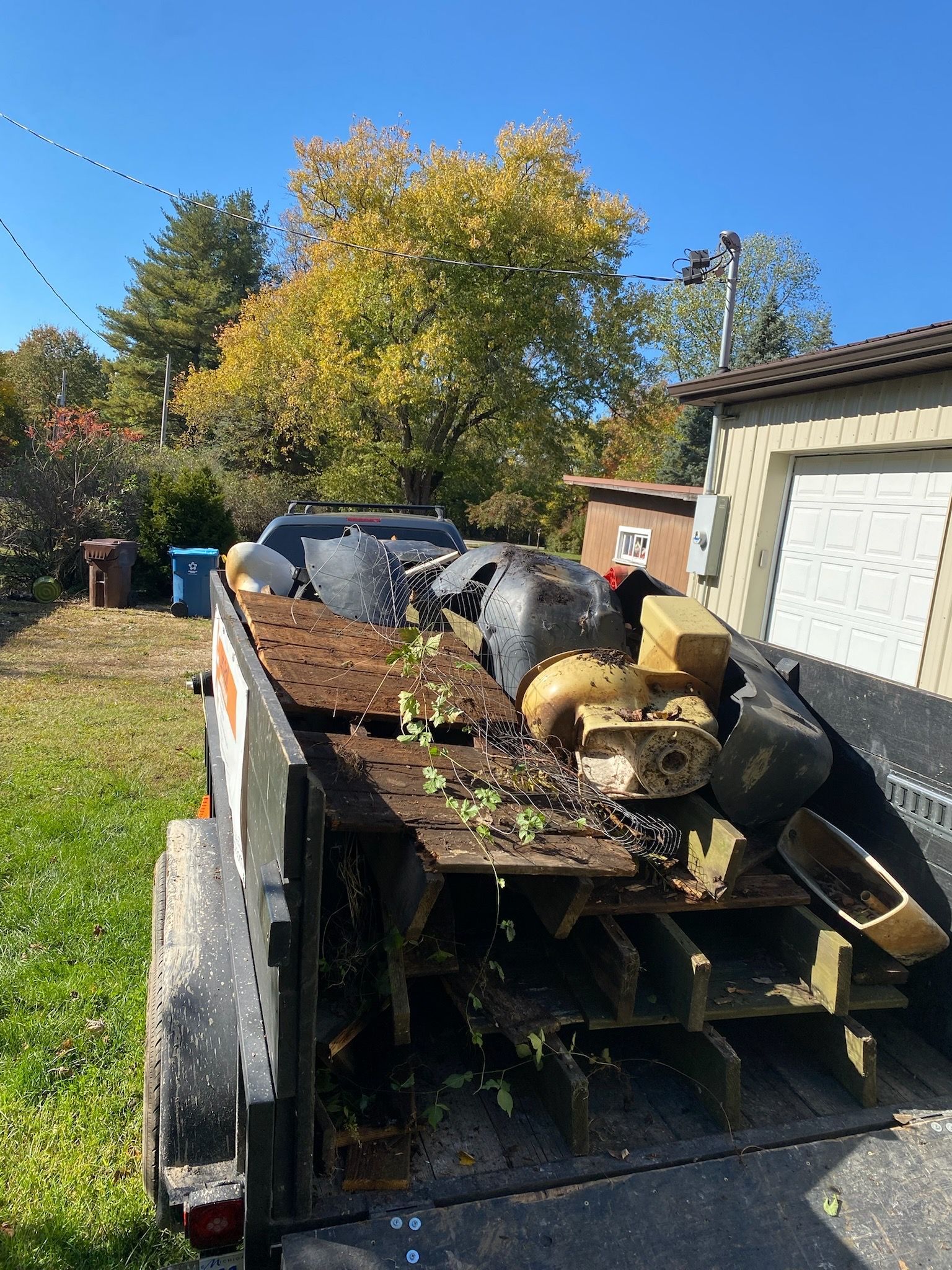 A trailer filled with junk is parked in front of a garage.