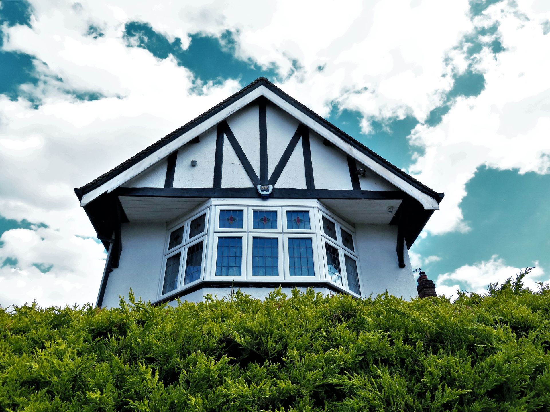 Black-and-white Tudor-style house above dense green shrubs under a cloudy sky
