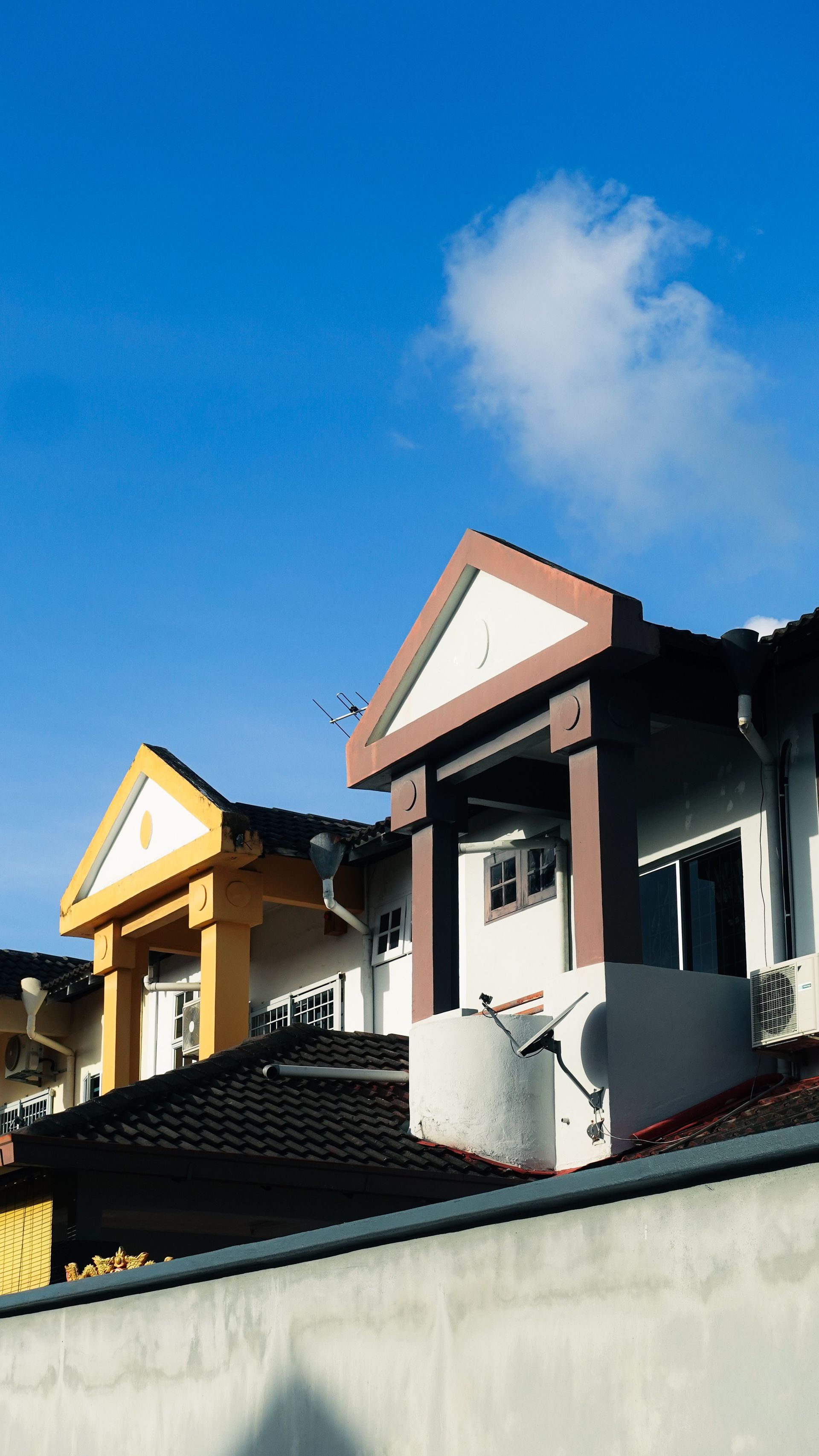 Colorful house rooftops with triangular dormers against a bright blue sky and a small cloud