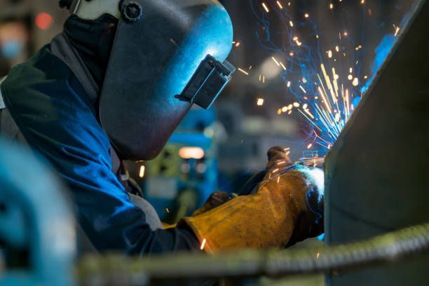 A person wearing a welding mask, and yellow gloves is performing steel welding services.