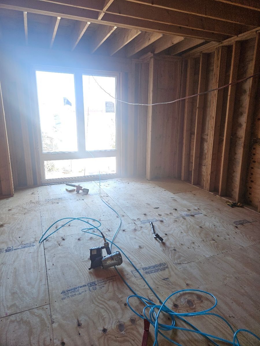 Interior renovation project showing open floor with plywood subfloor and exposed window framing