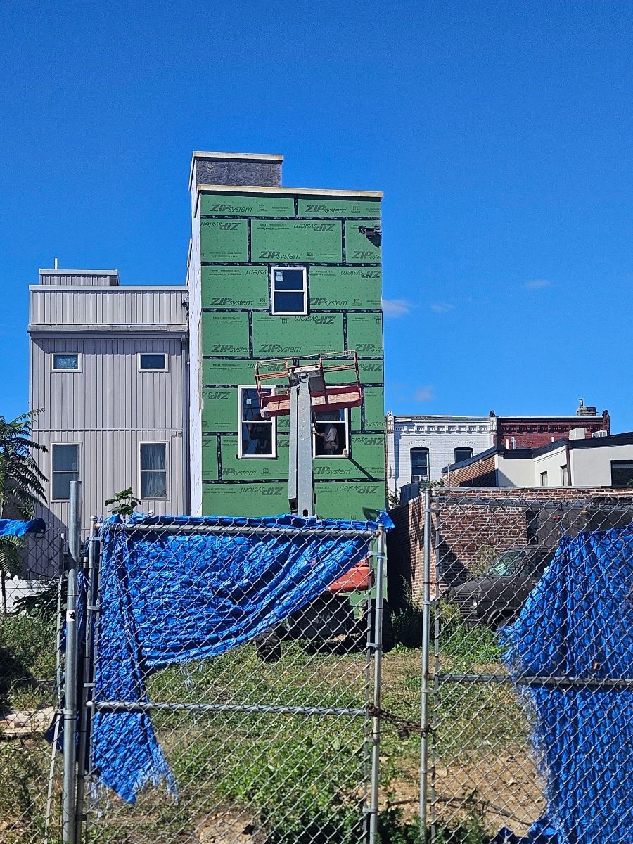 Street view of residential infill construction project wrapped in green ZIP System panels with safety fencing