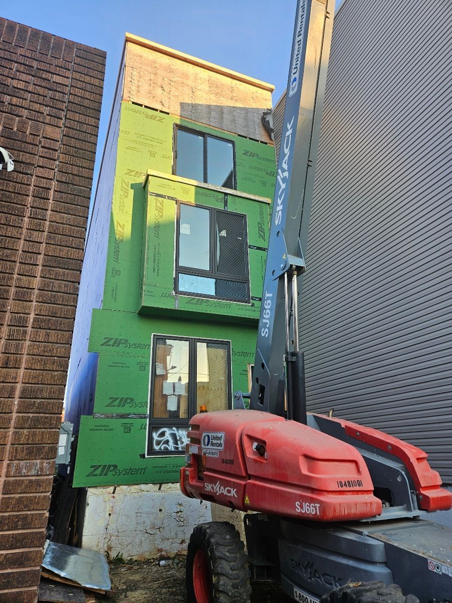 SkyJack lift positioned in front of new residential build with green sheathing, mid-construction