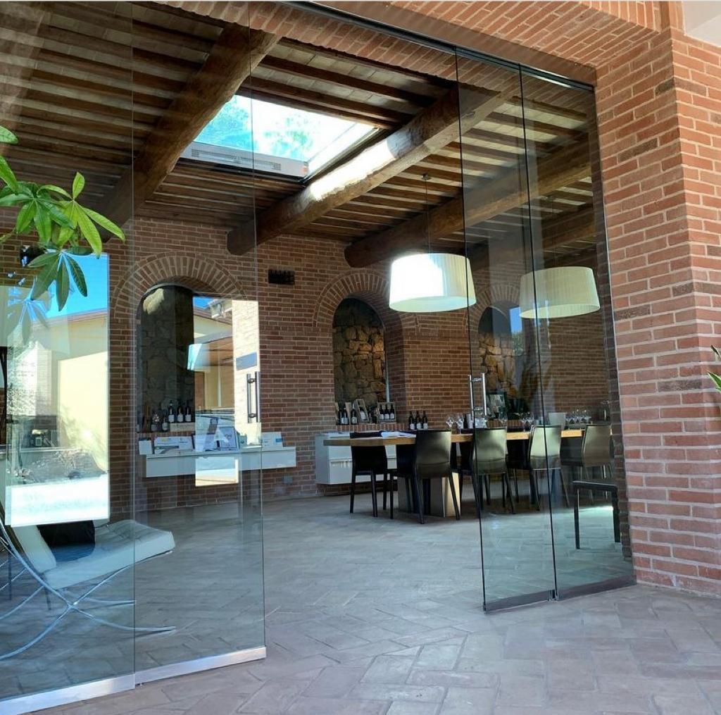 Zona pranzo esterna in mattoni con porte a vetri, travi in ​​legno a vista e un lungo tavolo all'interno.