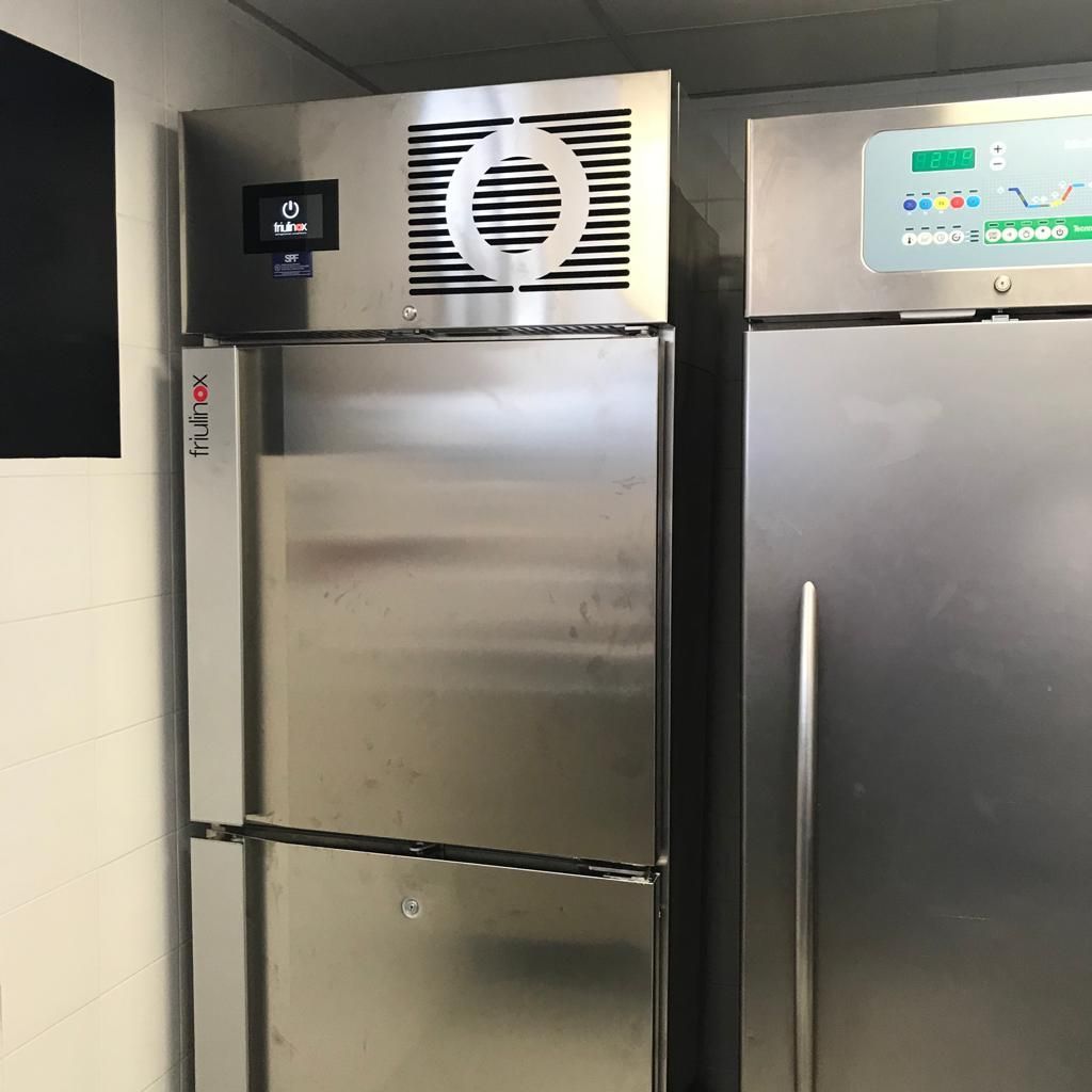 Frigorifero commerciale in acciaio inox in cucina, con cappa aspirante e comandi digitali sulla parte superiore.