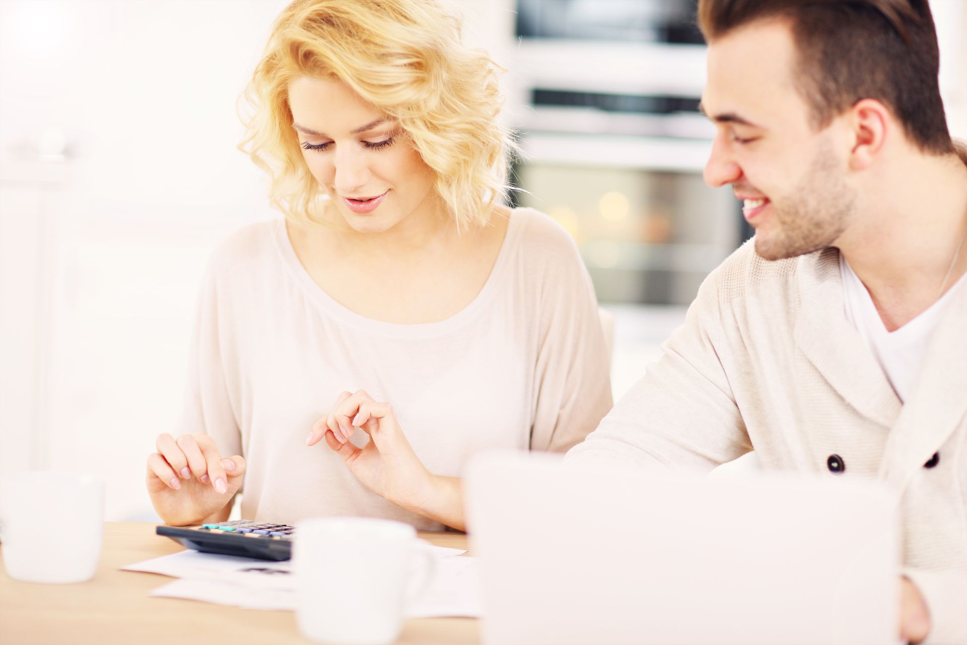 Couple calculating finances with a calculator and laptop, focused, in a kitchen.