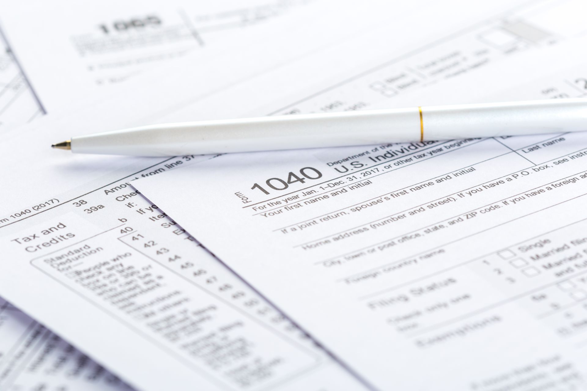 White pen rests on stacked tax forms, including a 1040 form.